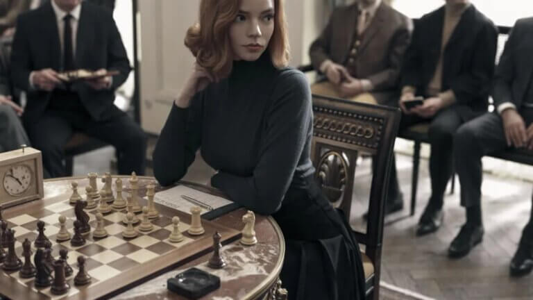The image shows actress Anya Taylor-Joy with a Staunton chess set in a scene from the Netflix series, The Queen's Gambit. Source: https://wallpapers.com/wallpapers/the-queen-s-gambit-match-with-borgov-t8sza5tnrrpch0hz.html